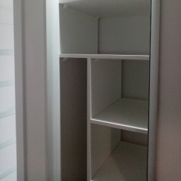 Adam Baczmański - Wnętrze białej, pustej szafy wnękowej z półkami, widok z bliska na pionowe i poziome przegrody.