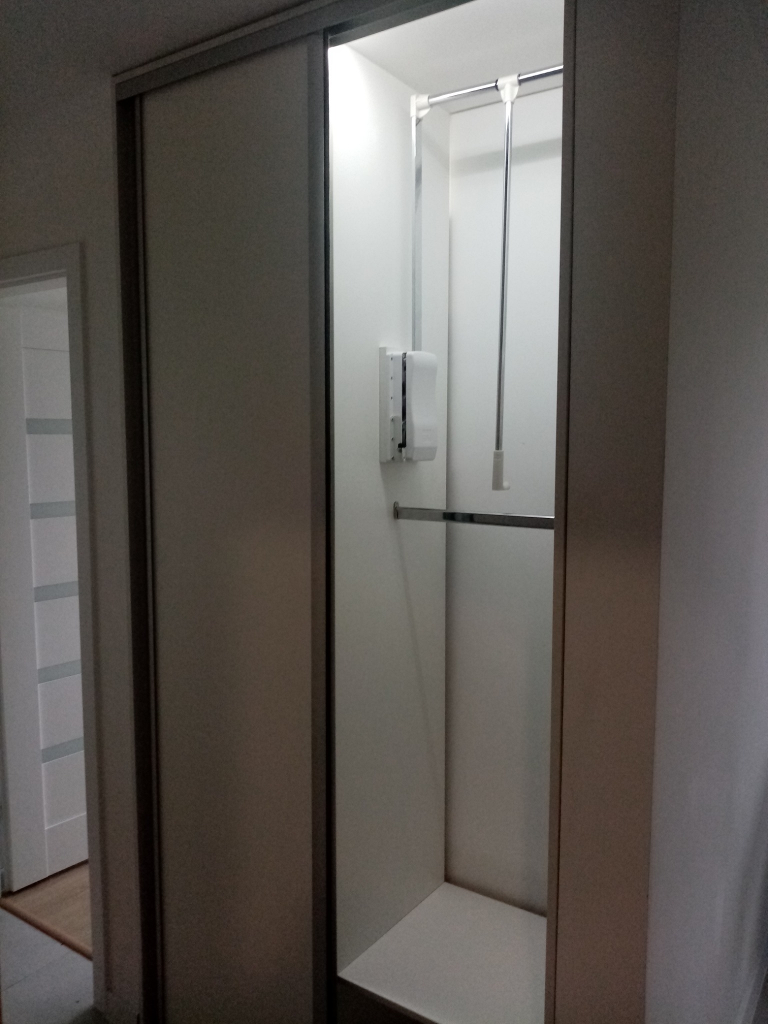 Wnętrze szafy wnękowej z przesuwnymi drzwiami, widoczny system drążków na ubrania i półka, oświetlenie wewnętrzne, dozownik na ścianie.