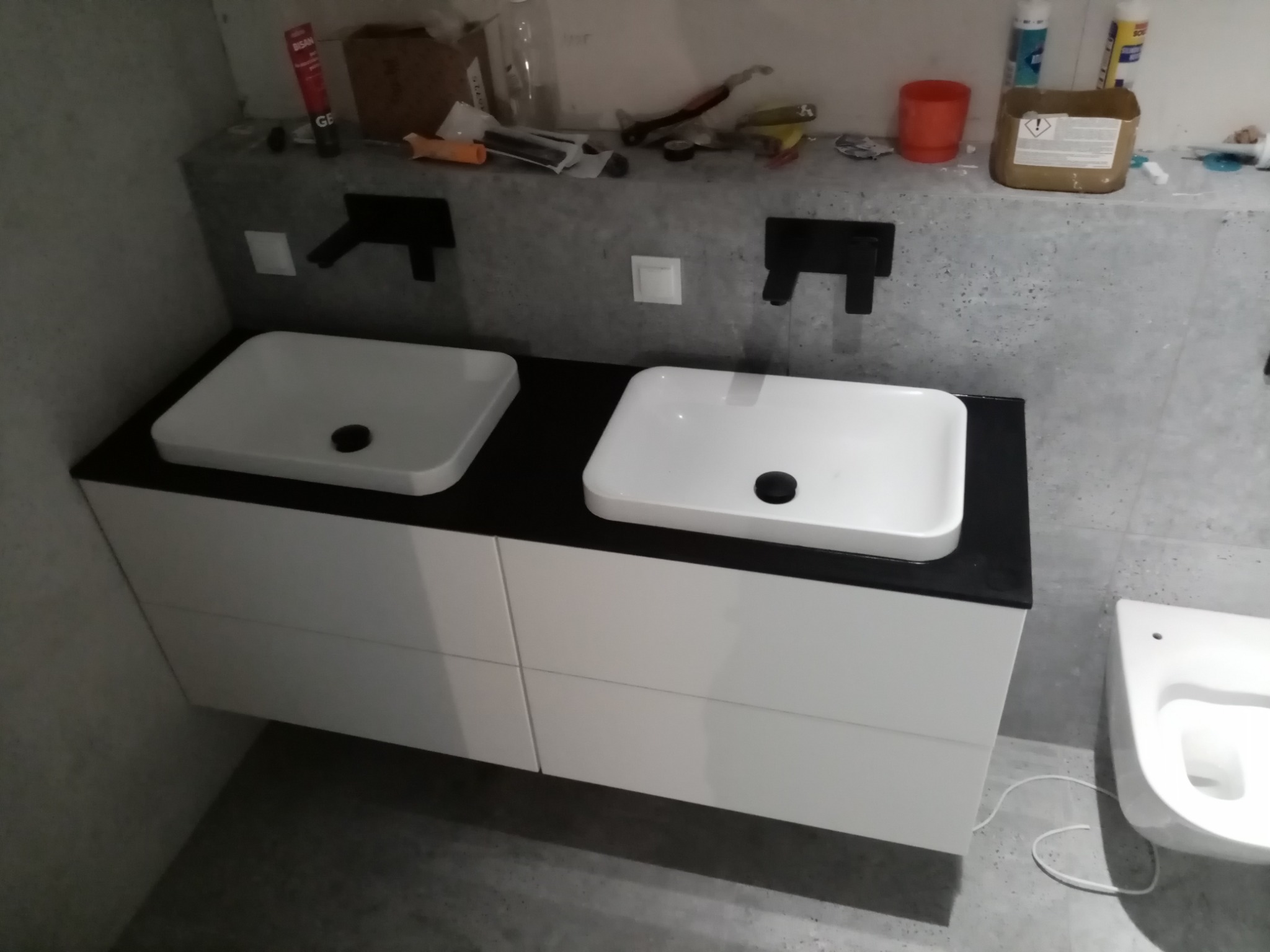 Nowoczesna łazienka we Wrocławiu z podwójną białą umywalką nablatową na szafce z białymi frontami, czarnym blatem i wiszącą toaletą.