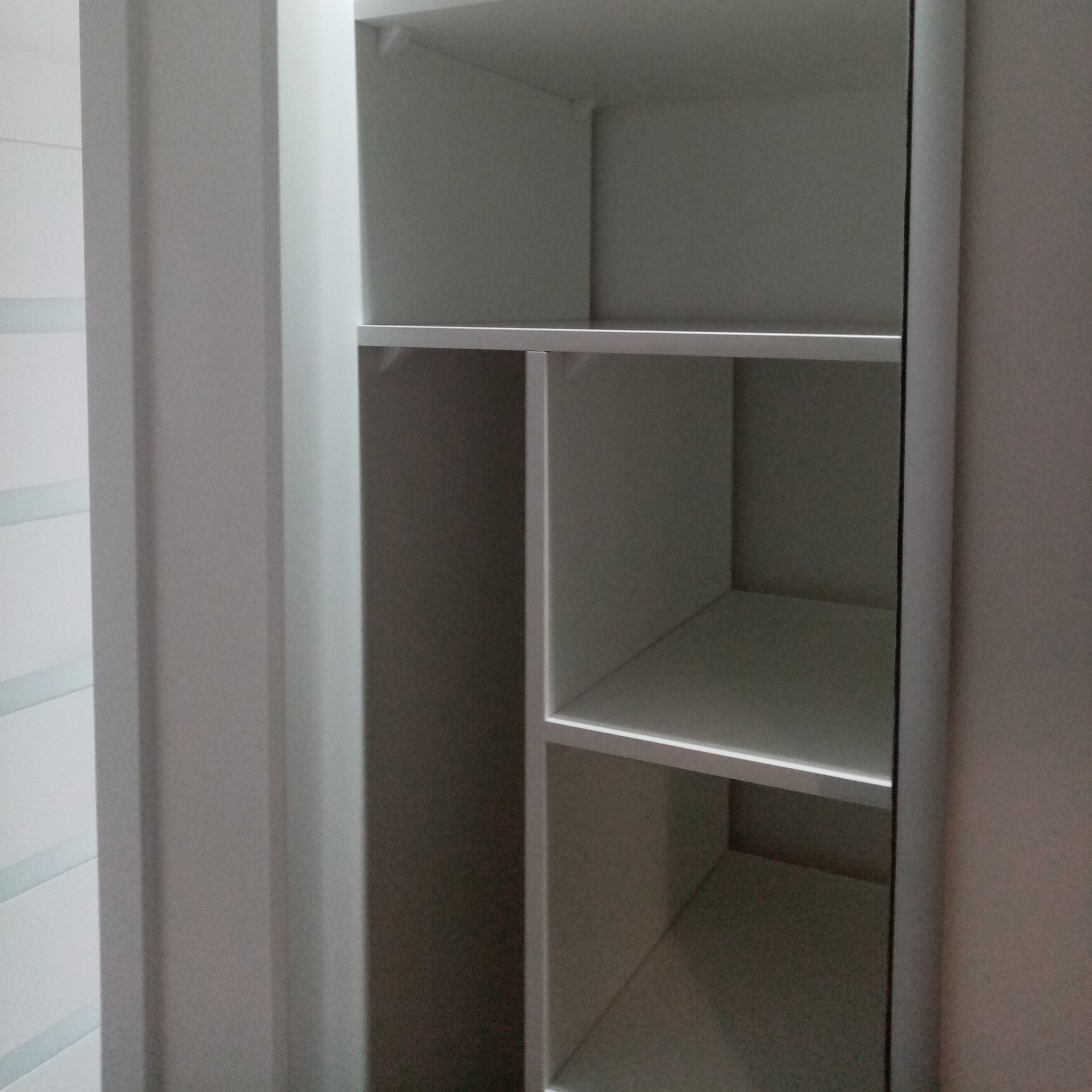 Wnętrze białej, pustej szafy wnękowej z półkami, widok z bliska na pionowe i poziome przegrody.