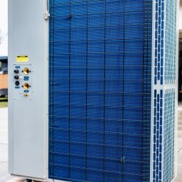 MS Power Sp. z o.o. - Zewnętrzna jednostka pompy ciepła, umieszczona na drewnianej palecie, z widocznymi przyłączami hydraulicznymi i elektrycznymi.