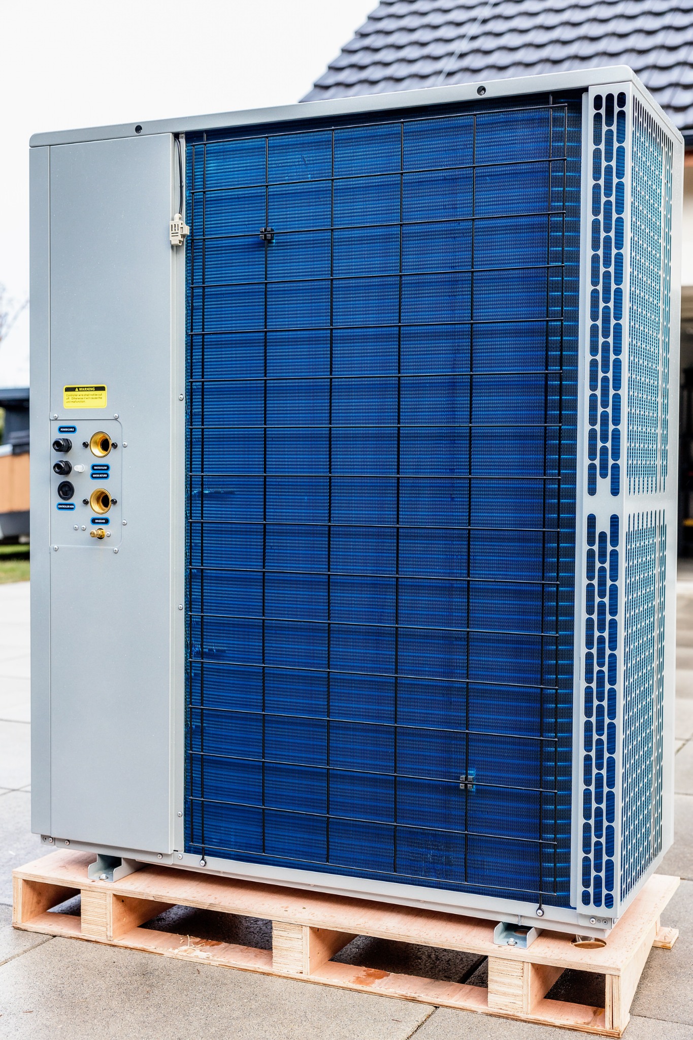 Zewnętrzna jednostka pompy ciepła, umieszczona na drewnianej palecie, z widocznymi przyłączami hydraulicznymi i elektrycznymi.