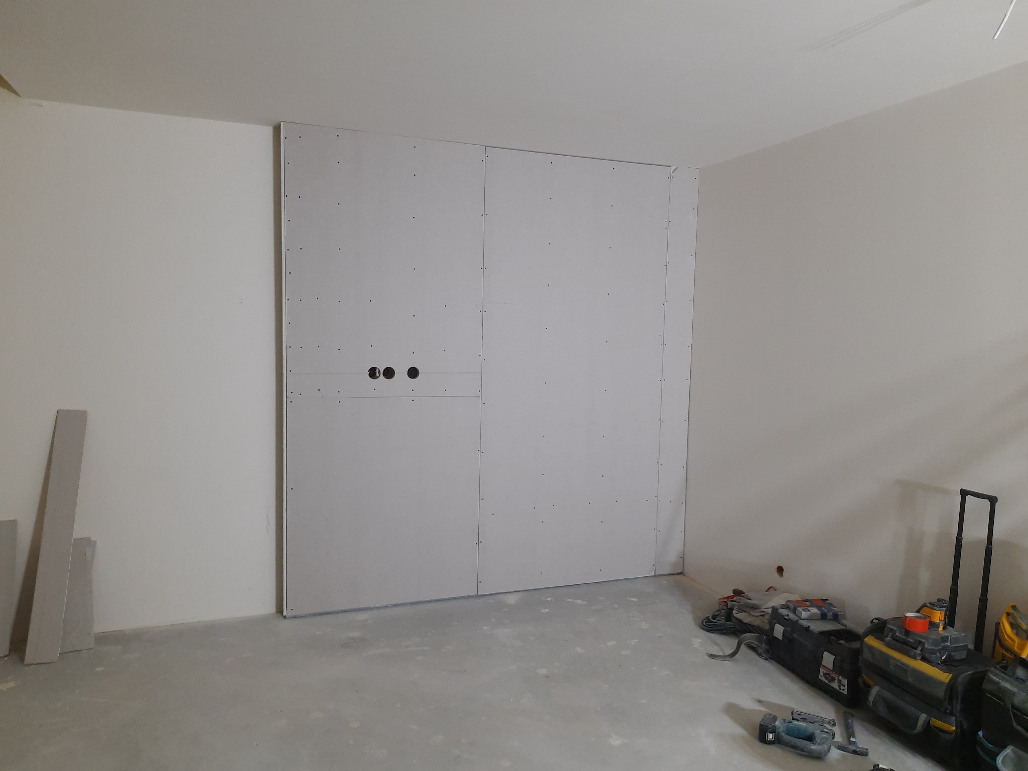 Montaż ściany działowej z płyt gipsowo-kartonowych z widocznymi otworami na instalacje elektryczne, narzędzia budowlane leżące na posadzce.