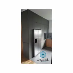 Nowoczesna kuchnia z szarymi szafkami zabudowanymi od podłogi do sufitu, zintegrowana z dwudrzwiową lodówką ze stali nierdzewnej, widok na fragment blatu i piekarnik w tle.