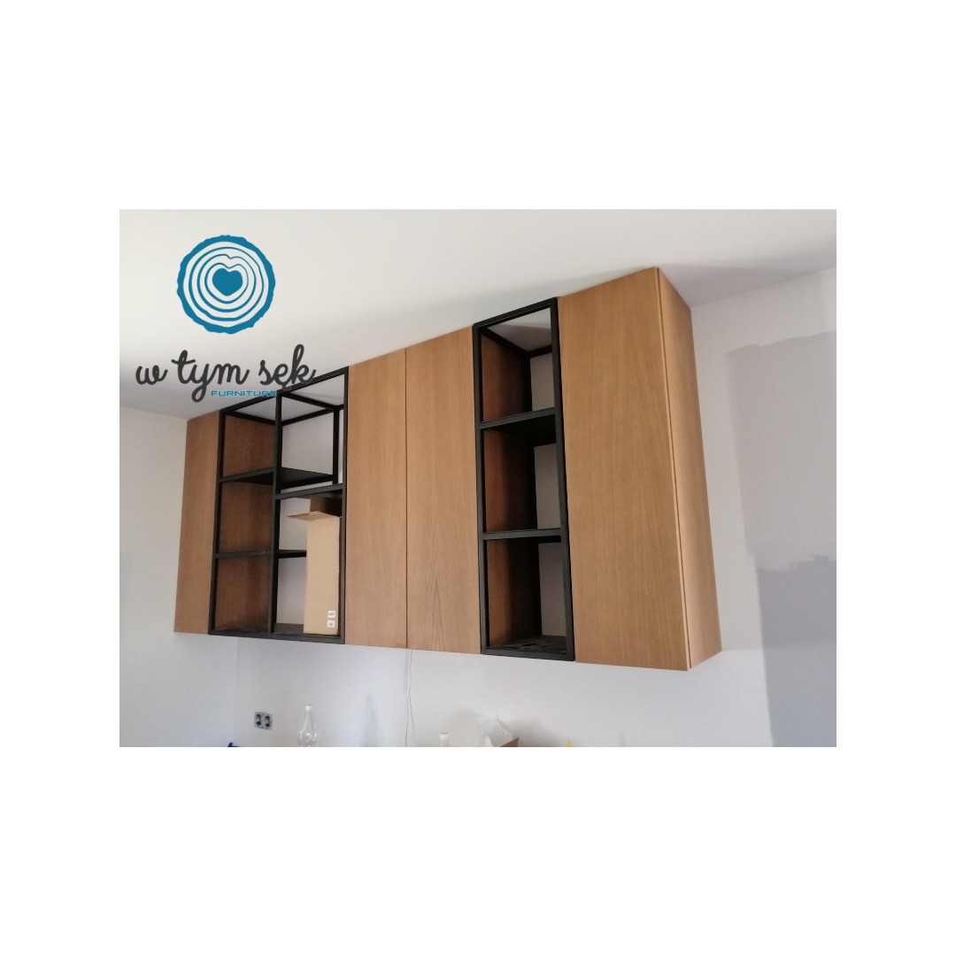 Wiszące szafki kuchenne z drewnianymi frontami i czarnymi, metalowymi półkami, widoczne logo firmy na ścianie, ściana w trakcie wykończenia.