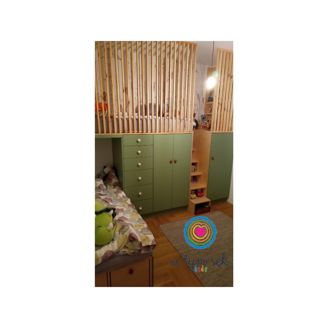 Pokój dziecięcy z łóżkiem na antresoli, zielonymi szafkami z gwiazdkami jako uchwytami i drewnianą barierką z pionowych listewek.