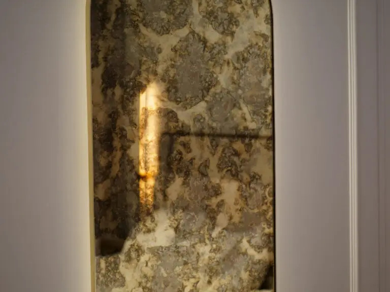 Fragment drzwi z dekoracyjnym, postarzanym lustrem wstawionym w panel, z odbijającym się światłem.