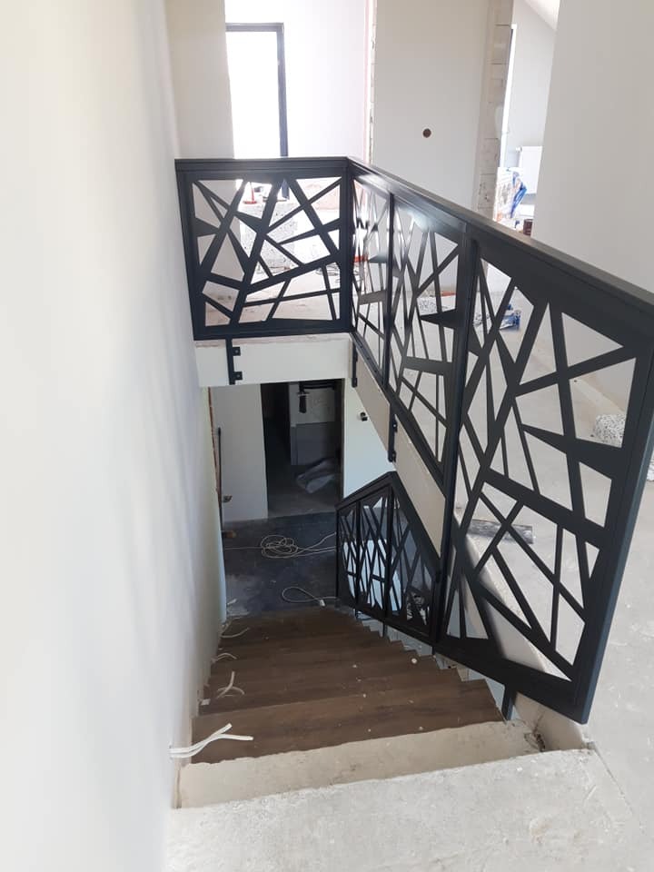 Klatka schodowa z nowoczesną, czarną balustradą o geometrycznym wzorze, widok z góry, częściowo wykończone wnętrze w trakcie remontu.