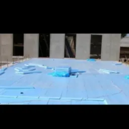 Płyty termoizolacyjne w kolorze błękitnym rozłożone na płaskim dachu budynku w trakcie budowy, widoczne otwory okienne w surowej konstrukcji.