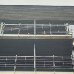 Robert Łaszczewski - Dwa balkony z metalowymi balustradami w Suchym Dębie, widok z dołu na elewację budynku z drewnianą okładziną.