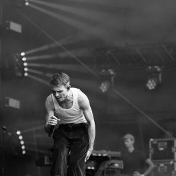 Nadia Wadelska - Czarno-białe zdjęcie piosenkarza z mikrofonem na scenie oświetlonej reflektorami, w tle widoczny klawiszowiec.