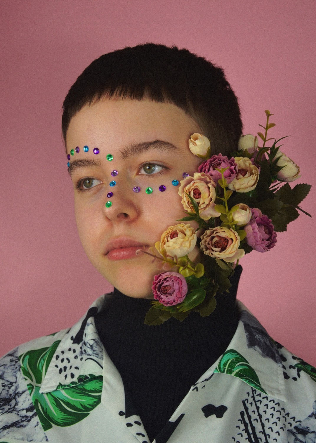 Portret osoby z dekoracjami z kwiatów i kolorowych kamieni na twarzy, na różowym tle.