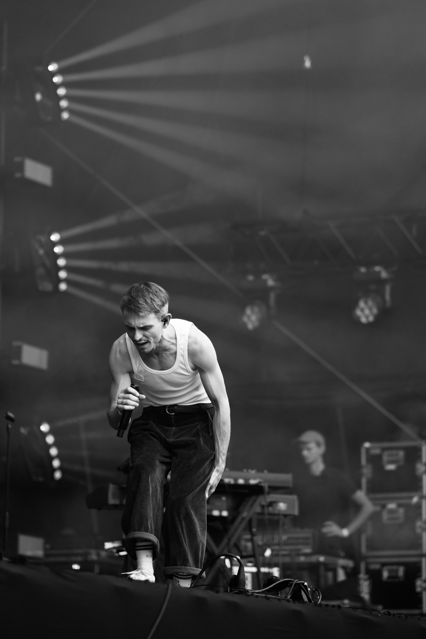 Czarno-białe zdjęcie piosenkarza z mikrofonem na scenie oświetlonej reflektorami, w tle widoczny klawiszowiec.