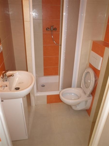 Jasna łazienka z kabiną prysznicową, umywalką na szafce i podwieszaną toaletą, wykończona beżowymi i pomarańczowymi płytkami w pionowe pasy.