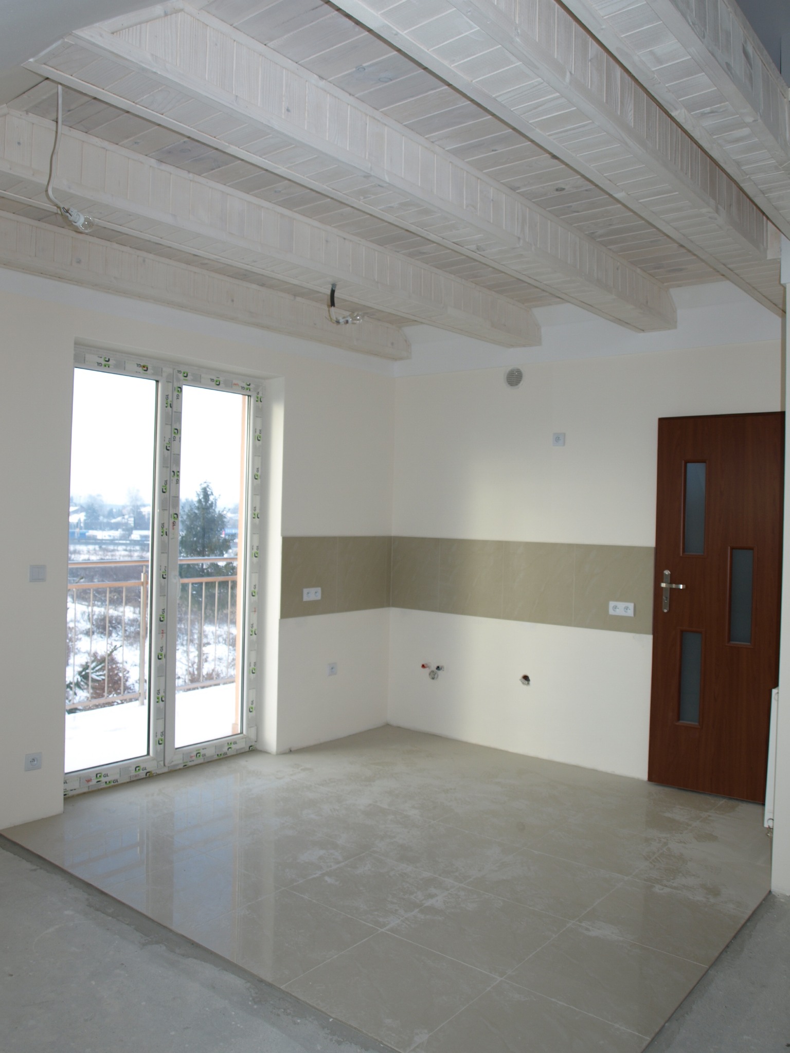 Wnętrze pokoju w Modlnicy z nową, jasną podłogą z płytek, drewnianym sufitem z widocznymi kablami i dużym oknem balkonowym z widokiem na zimowy krajobraz.