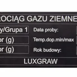 Tabliczka znamionowa rurociągu gazu ziemnego z informacjami technicznymi, datą próby, ciśnieniem, temperaturą i rokiem budowy, wykonana przez producenta LUXGRAW.