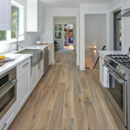 Nowoczesna kuchnia we Wrocławiu z białymi szafkami, marmurowym blatem, stalowym zlewem i sprzętem AGD, wykończona płytkami ułożonymi w jodełkę oraz drewnianą podłogą.