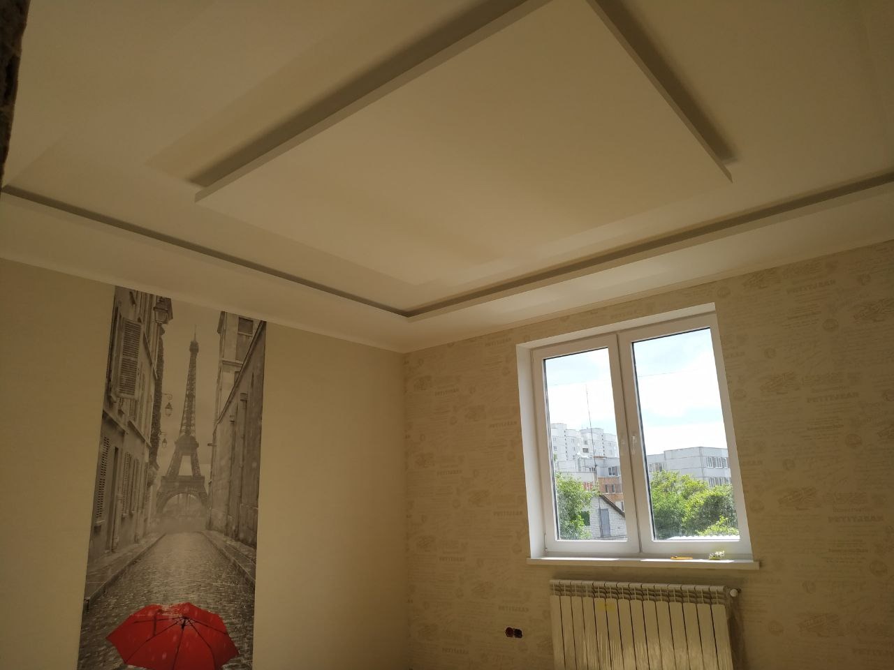 Pokój po remoncie: Sufit podwieszany z prostokątnym wgłębieniem, tapeta w delikatny wzór, fototapeta z widokiem na wieżę Eiffla i czerwonym parasolem, białe okno z widokiem na osiedle.