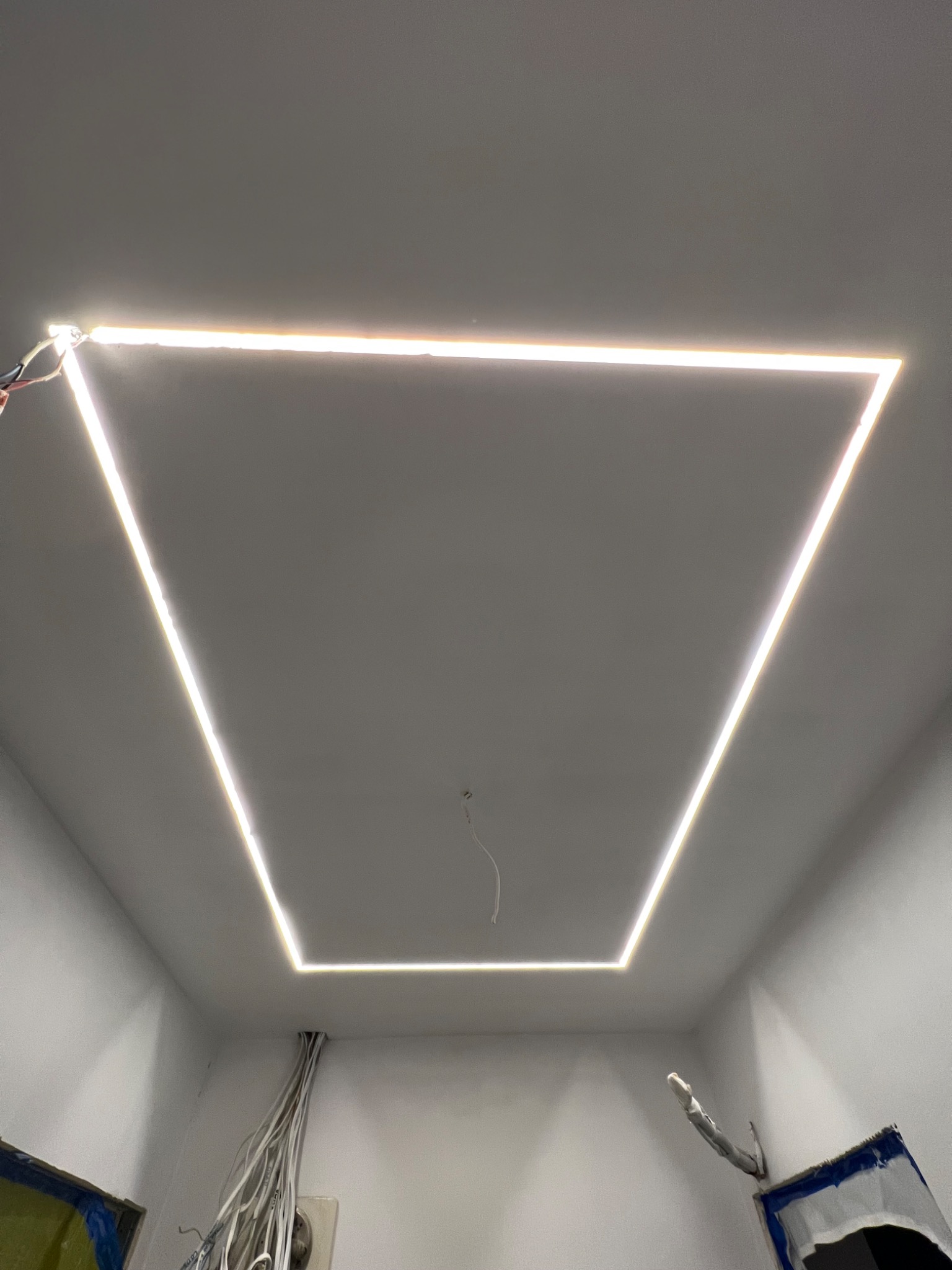 Podwieszany sufit z oświetleniem LED w kształcie trapezu, widoczne kable i niedokończone wykończenie ścian.