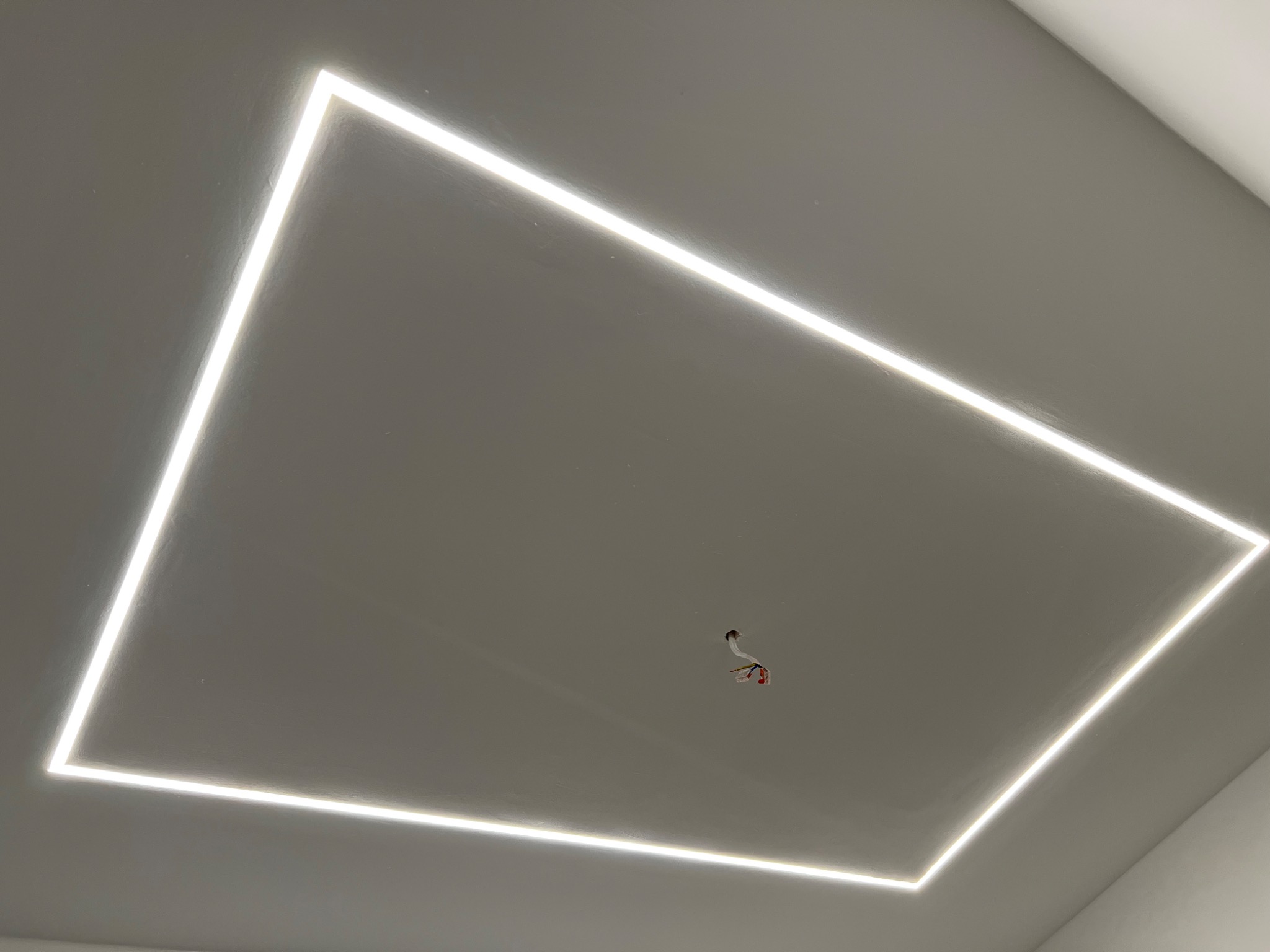 Nowoczesny sufit z wpuszczonym oświetleniem LED w kształcie prostokąta, widoczne wystające przewody elektryczne w centralnej części.