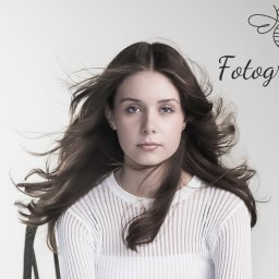 FOTOGRAFIKA Anna Pszczułkowska - Portret młodej kobiety z rozwianymi włosami na jasnym tle, z widocznym logo firmy fotograficznej w prawym górnym rogu.