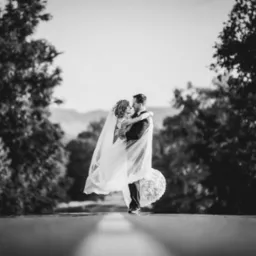 Czarno-białe zdjęcie pary młodej w objęciach na tle drzew i gór, panna młoda w długim welonie.