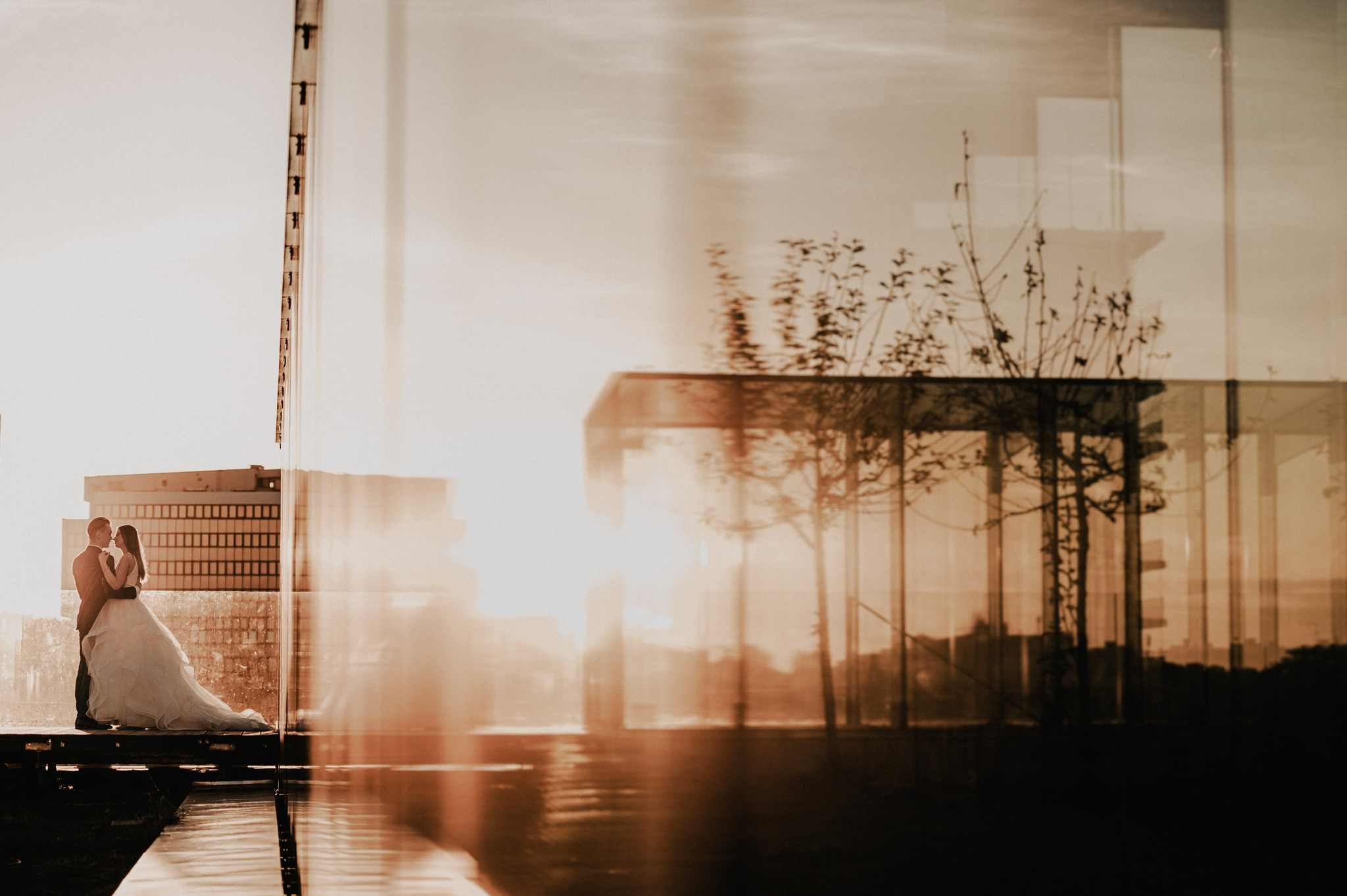 Para młoda w objęciach na tle nowoczesnej architektury i refleksji w wodzie, ciepłe światło słoneczne.