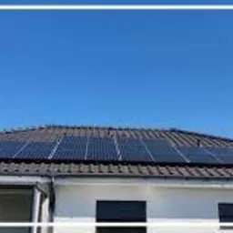 Panel słoneczny na dachu domu jednorodzinnego z widocznym logo firmy Helios System w lewym górnym rogu, błękitne niebo w tle.