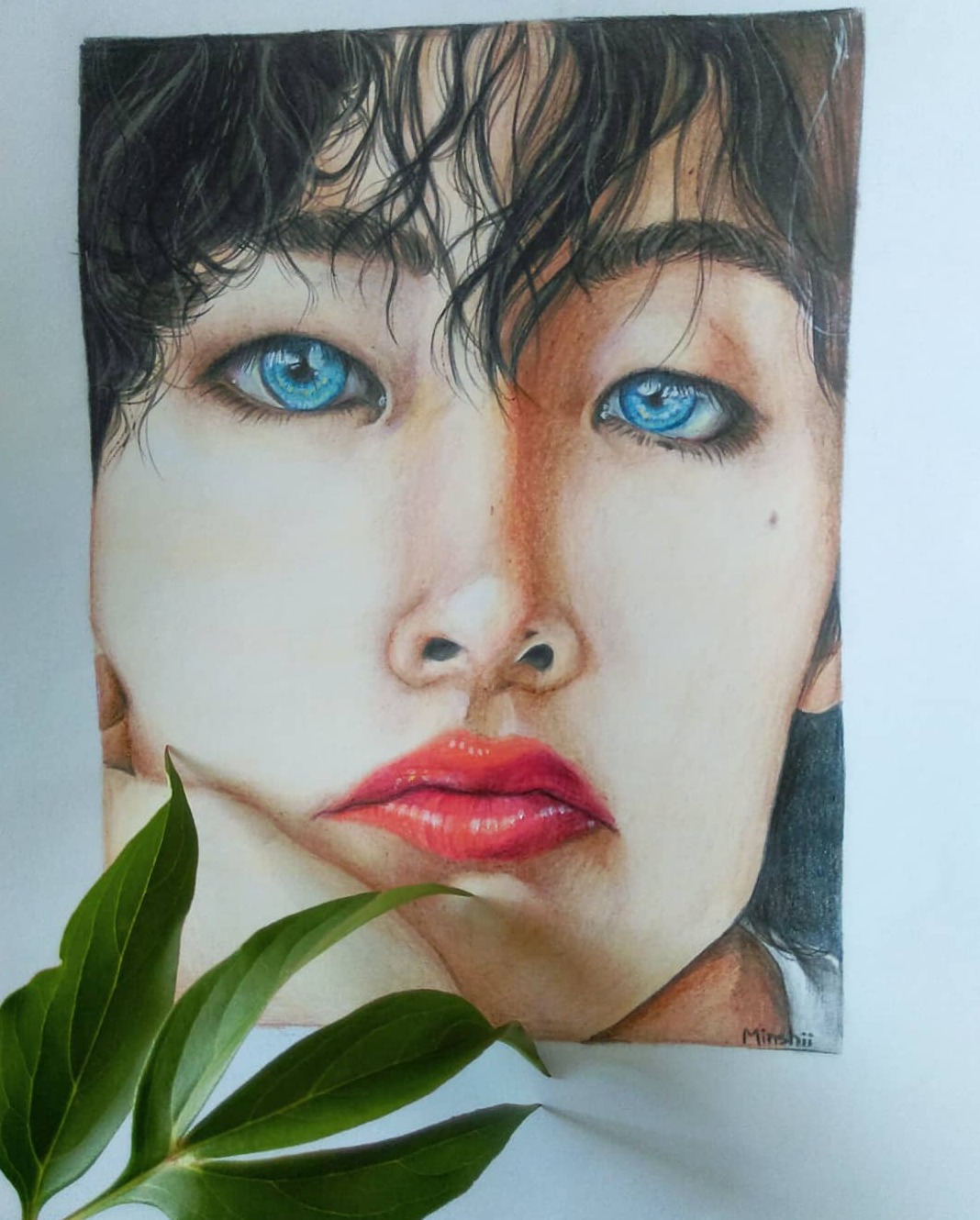 Portret osoby o jasnych oczach, wykonany kredkami na papierze, z zielonymi liśćmi w dolnym rogu.