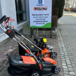 Dwie kosiarki spalinowe i elektryczne marki Husqvarna i Oleo-Mac przed salonem sprzedaży sprzętu ogrodowego Technika Trawnika z widocznym szyldem reklamowym.
