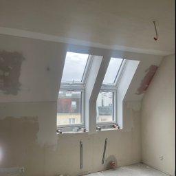 KondorBUD - Pokój na poddaszu w trakcie remontu. Widoczne okna dachowe, ściany w trakcie szpachlowania, fragment instalacji elektrycznej i resztki materiałów budowlanych na podłodze.