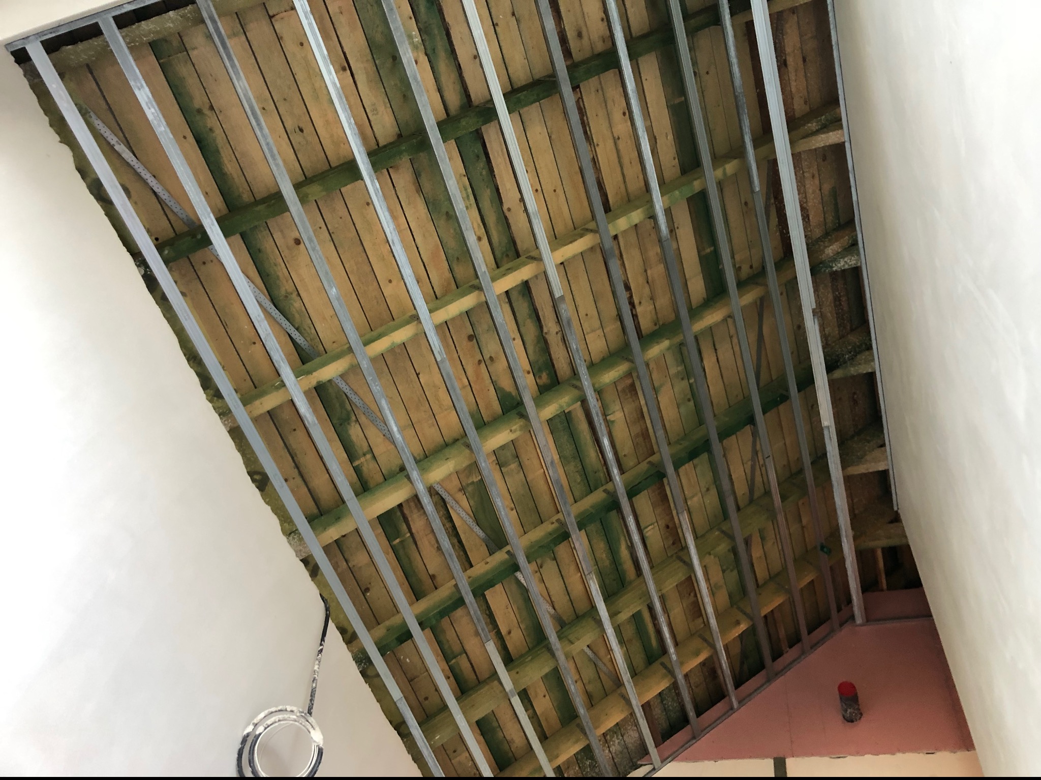 Skośny sufit z drewnianą konstrukcją i metalowymi profilami, przygotowany do montażu płyt karton-gips. Widoczne ocieplenie i fragment ściany. Ujęcie z dołu.