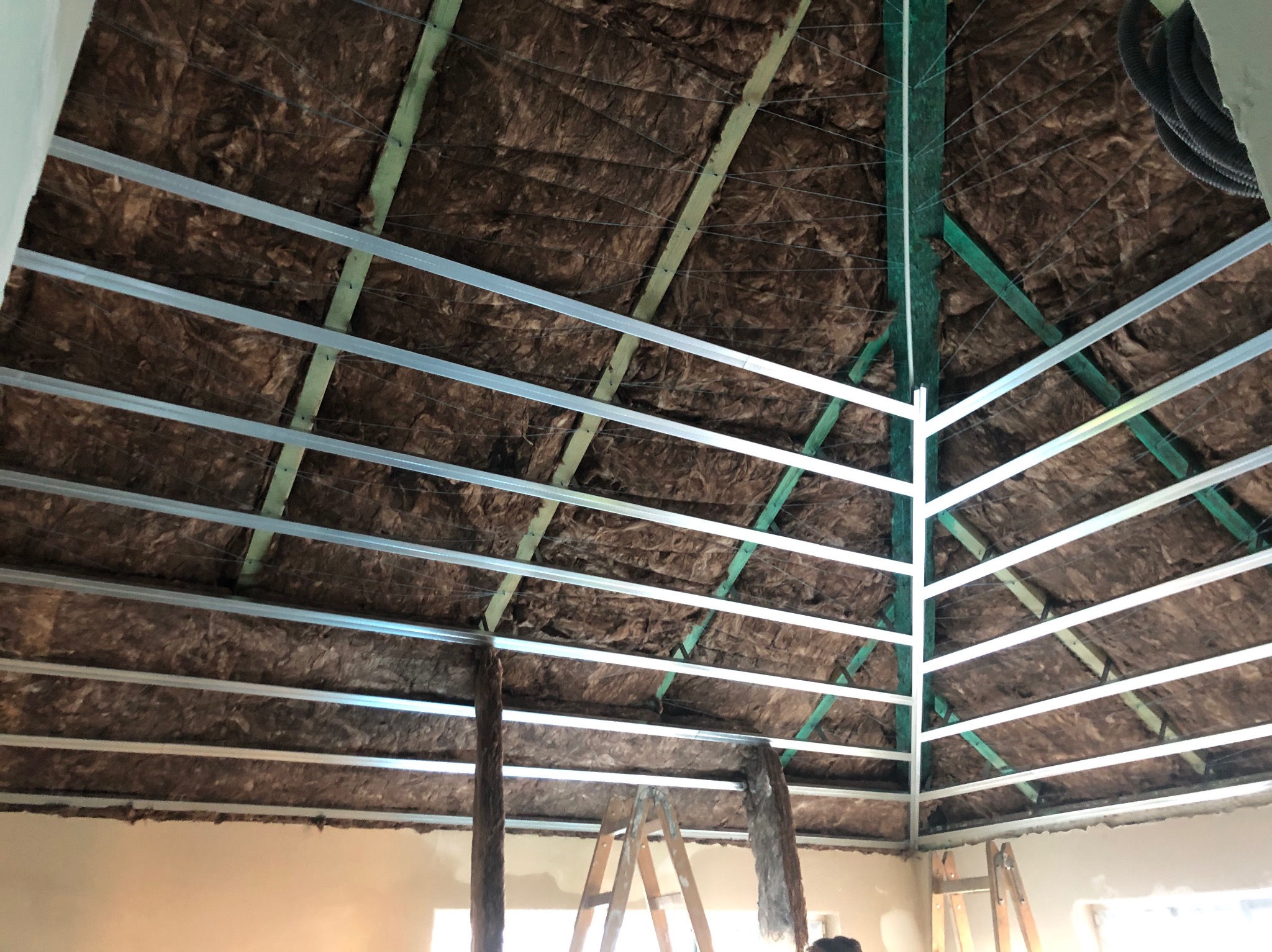 Skośny sufit poddasza z izolacją z wełny mineralnej, widoczne metalowe profile konstrukcyjne i drewniane elementy więźby dachowej. Etap prac wykończeniowych.