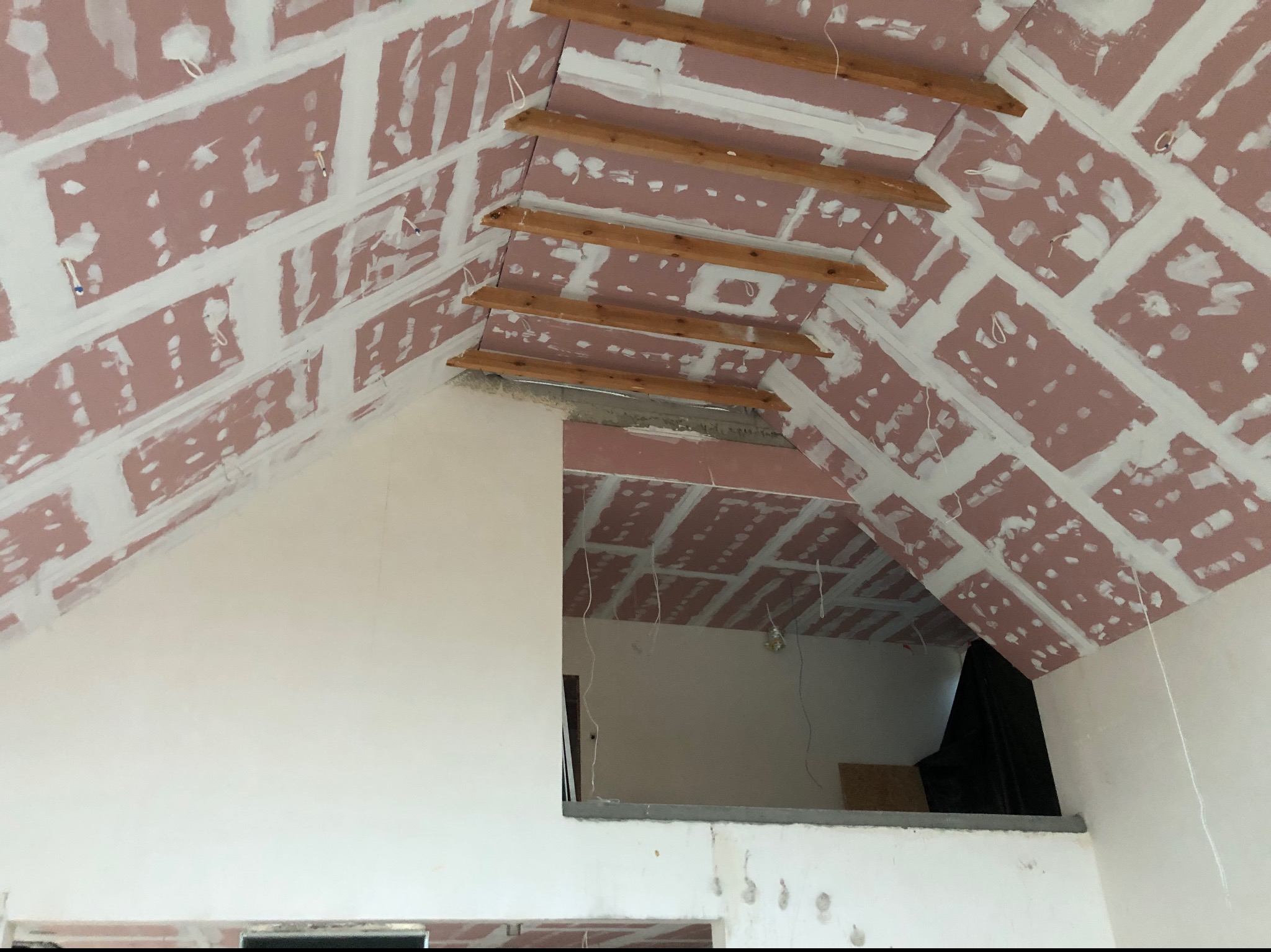 Skośny sufit poddasza z zamontowaną płytą karton-gips, widoczne drewniane belki i wstępnie wypełnione spoiny. Prace wykończeniowe w trakcie realizacji.