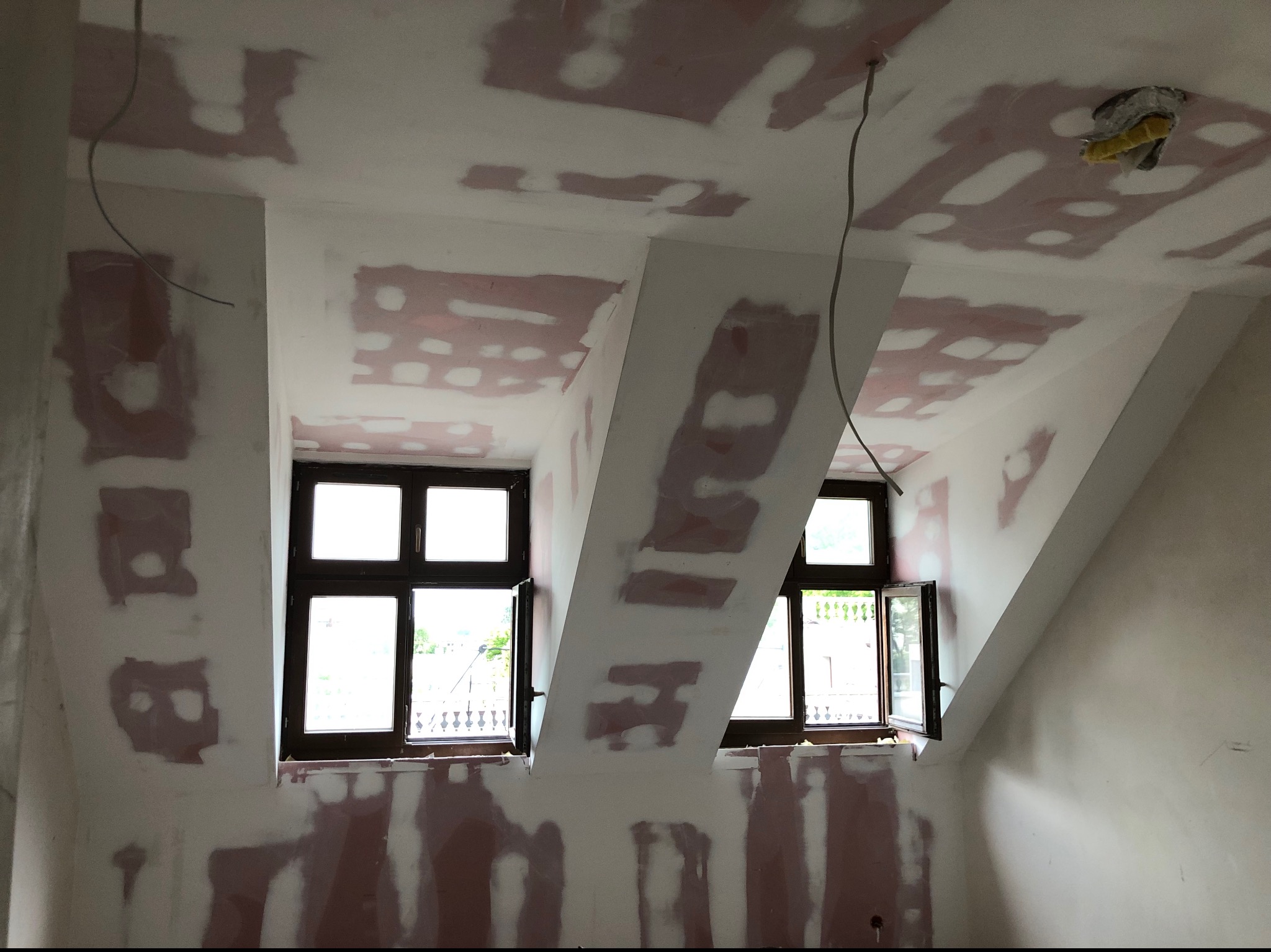 Sufit i ściany po szpachlowaniu we Wrocławiu, widoczne dwa okna. Prace przygotowawcze przed malowaniem w pomieszczeniu na poddaszu.