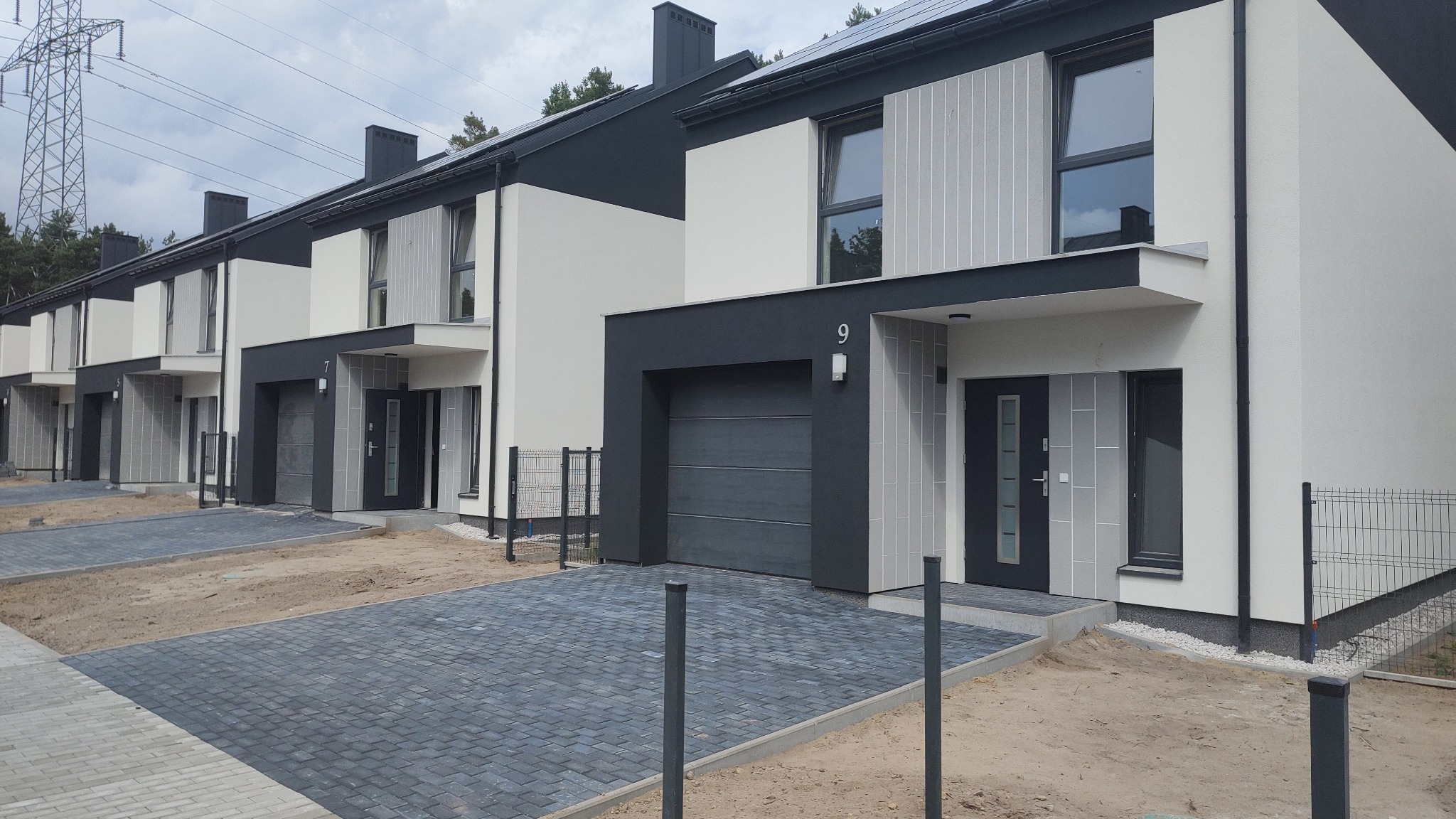 Nowoczesne domy w zabudowie szeregowej z szarej kostki brukowej na podjeździe, widok z poziomu gruntu na ukończony projekt.