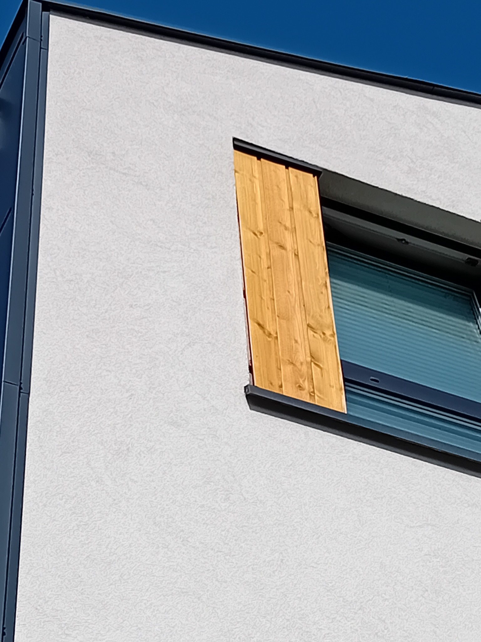 Nowoczesne okno drewniane z żaluzjami i drewnianą osłoną, widok z dołu na tle błękitnego nieba.