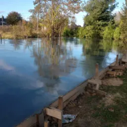 Świeżo wylana, gładka wylewka anhydrytowa z drewnianym szalunkiem w otoczeniu zieleni i drzew, odbijająca niebo.