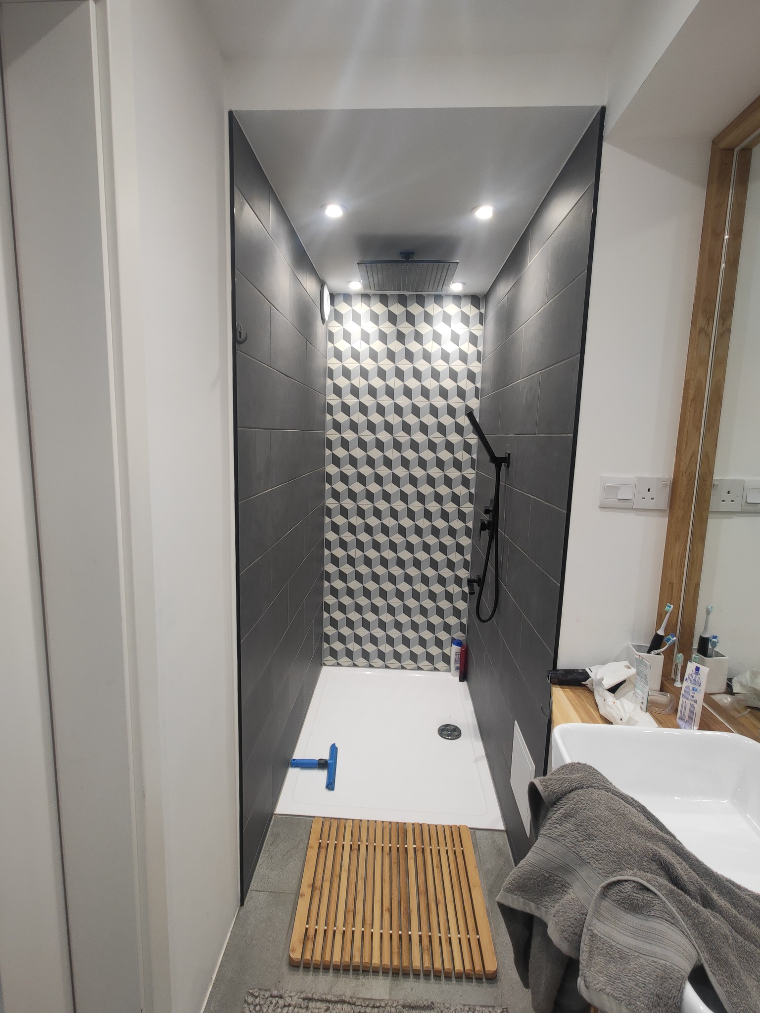 Nowoczesna kabina prysznicowa z geometrycznym wzorem na ścianie w Doncaster, widok od wejścia, z drewnianą wycieraczką i szarą płytką podłogową.