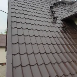 Nowy, brązowy dach z blachodachówki modułowej z zamontowanymi stopniami kominiarskimi i zabezpieczonym kominem.