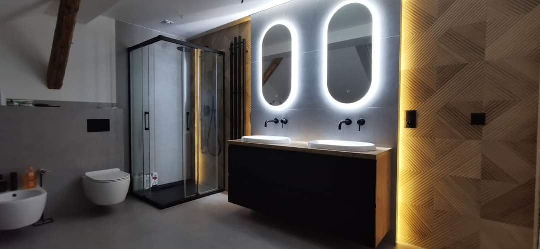 Nowoczesna łazienka z kabiną prysznicową w czarnej ramie, podwójną umywalką na czarnej szafce z drewnianym blatem, podświetlanymi lustrami owalnymi i dekoracyjną ścianą z geometrycznym wzorem...