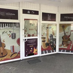 Okna Iławskiego Centrum Kultury oklejone grafikami z motywami muzycznymi, promujące festiwale i wydarzenia kulturalne, widok z zewnątrz.