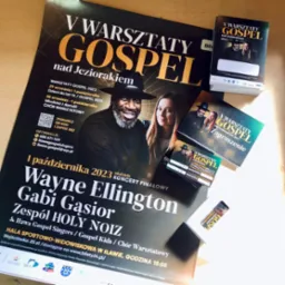 Stos ulotek i zaproszeń na V Warsztaty Gospel nad Jeziorakiem 2023, z wizerunkami Wayne'a Ellingtona i Gabi Gąsior z Zespołu Holy Noiz, na tle plakatu informacyjnego.