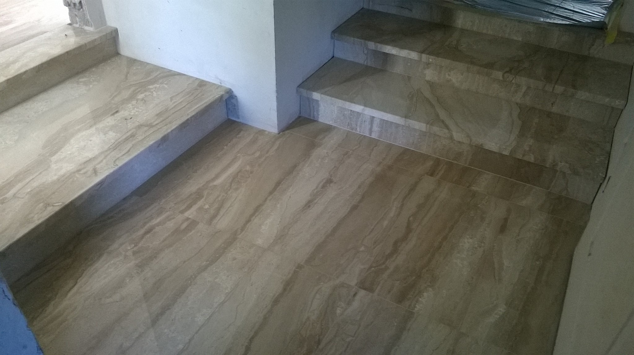 Ułożone płytki imitujące marmur na podłodze i schodach wewnątrz budynku, widoczne fugi i kąt nachylenia schodów.