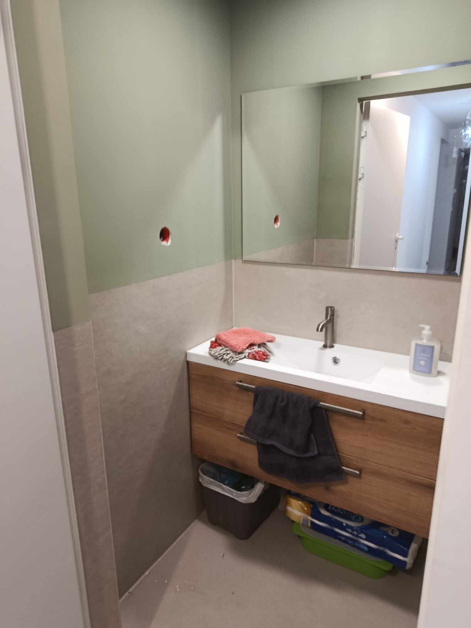 Łazienka w trakcie wykańczania: umywalka z drewnianą szafką, lustro, częściowo pomalowane ściany z widocznymi otworami na gniazdka.