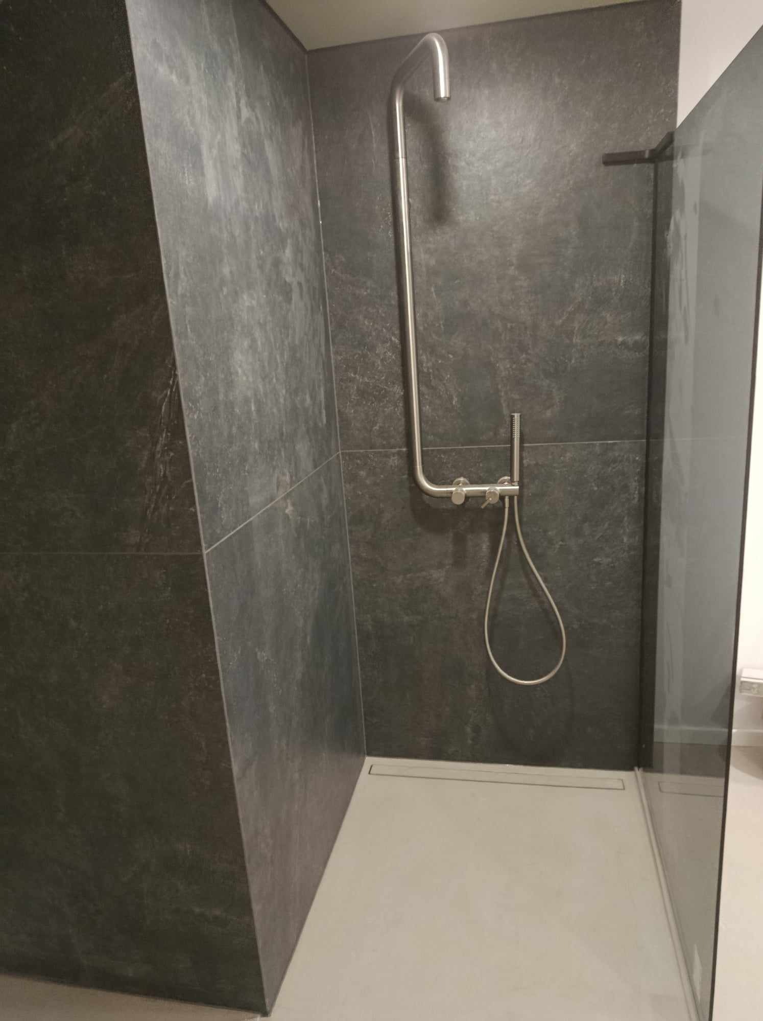 Nowoczesna kabina prysznicowa walk-in z ciemnoszarą, kamienną okładziną ścian i minimalistyczną armaturą ze stali nierdzewnej.