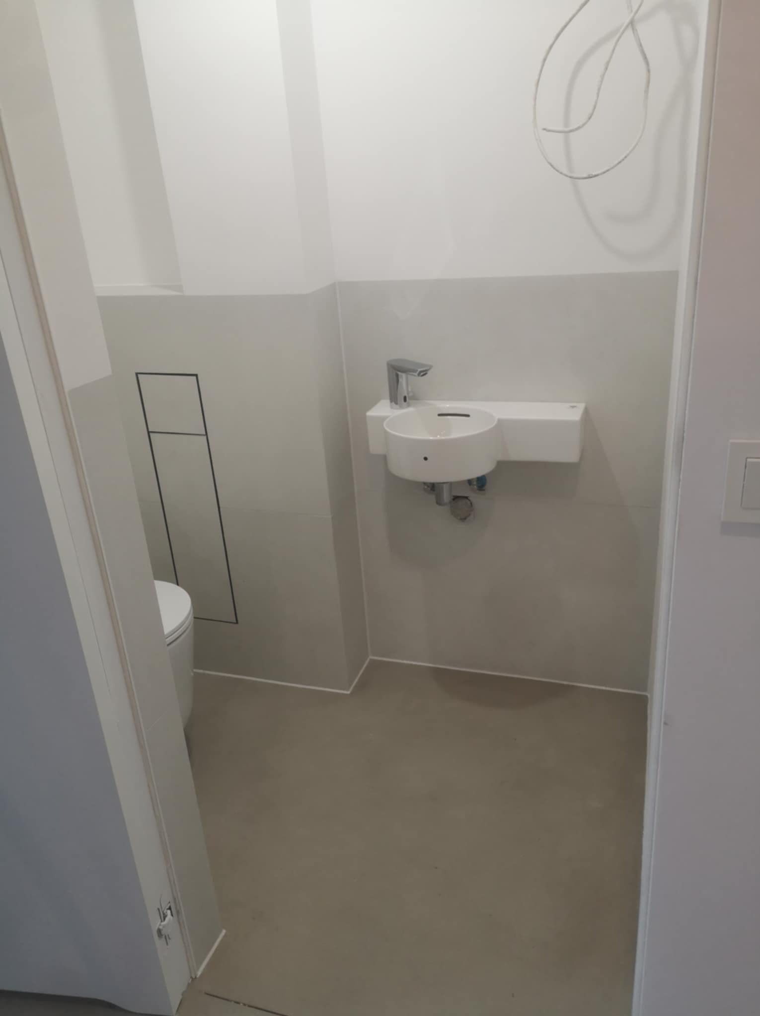 Nowoczesna, minimalistyczna łazienka w Borne Sulinowo z białą umywalką nablatową i szarą glazurą, widoczne niedokończone podłączenie elektryczne na suficie.