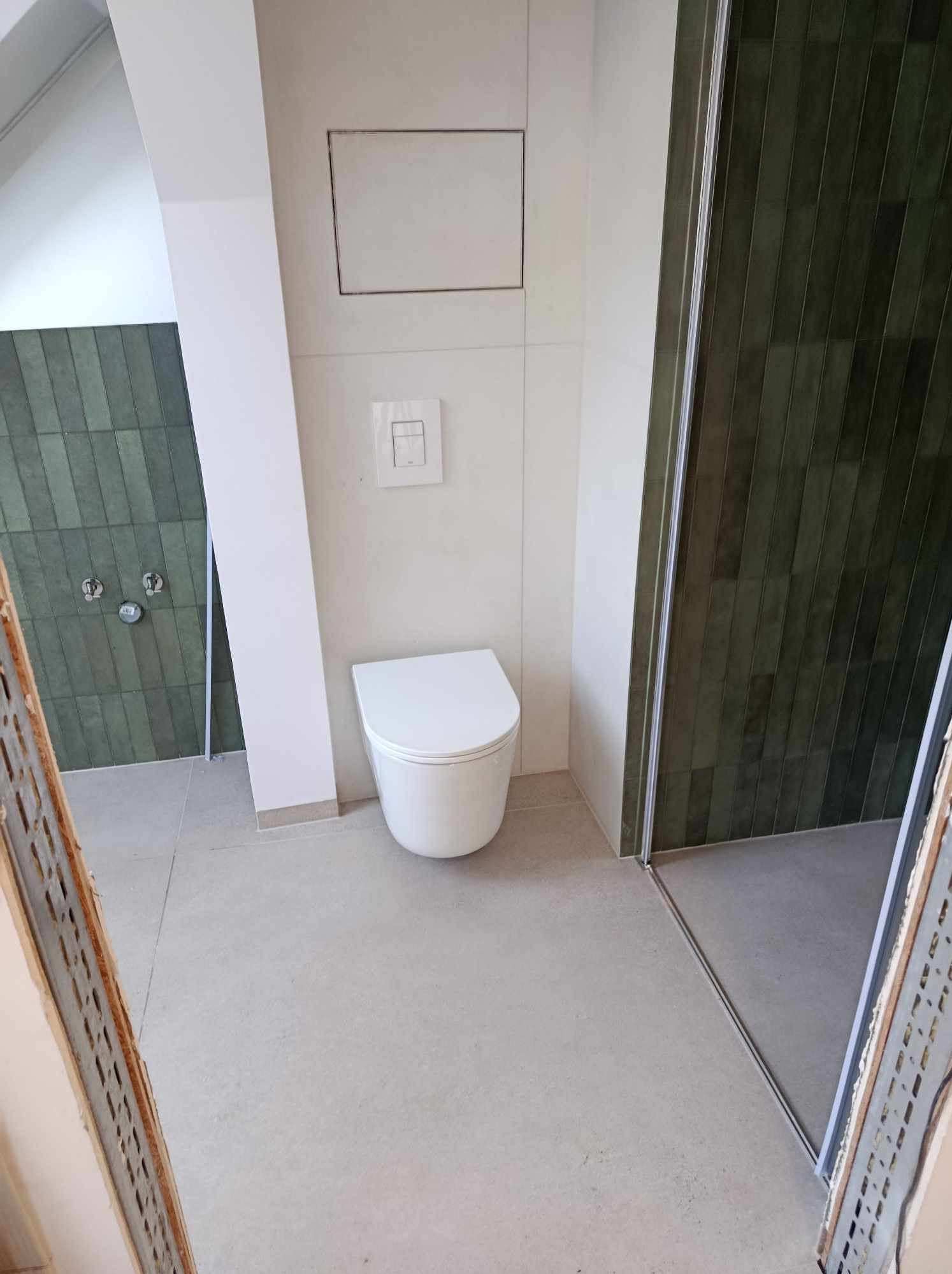 Nowoczesna łazienka w odcieniach bieli i butelkowej zieleni z wiszącą toaletą, płytkami ułożonymi pionowo i kabiną prysznicową ze szklanymi drzwiami.