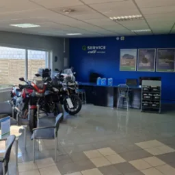 Wnętrze salonu motocyklowego CWS Piekarski z trzema motocyklami w strefie oczekiwania, niebieska ściana z logo i reklamami Castrol oraz półki z akcesoriami.