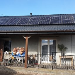 Lub-eko Sp. z o.o. - Dom jednorodzinny z panelami słonecznymi na dachu, widoczny traktor z przyczepą drewna w tle, balkon z metalową balustradą i drewnianymi słupami.